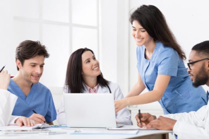 Medical personnel working together at a table. There is one person working on a laptop while others take notes in a notebook.