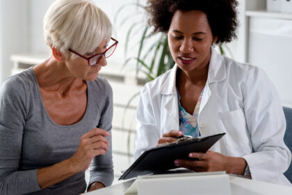 Dietitians speaks to a patient while reviewing notes on a clipboard