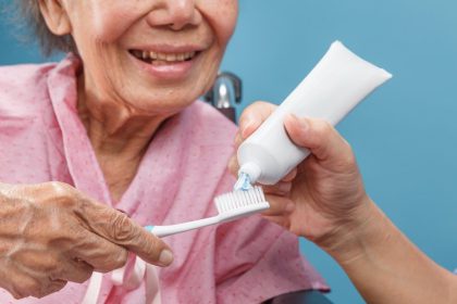 person squeezing tooth paste onto tooth brush for elderly lady